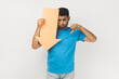 © khosrork - Disappointed unshaven man wearing blue T- shirt standing holding paper arrow indicating down, looking at camera with sad expression, showing thumb down. Indoor studio shot isolated on gray background.