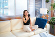 © Stella 16 - Young smiling woman sitting on sofa at home and taking selfie