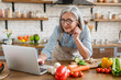 © InsideCreativeHouse - Mature woman multitasking in kitchen, cooking breakfast meal lunch, preparing food, tasty dinner salad at home kitchen while using laptop with online tutorial, browsing healthy meal recipe on Internet