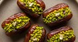 © Adi - Delicious dates stuffed with vibrant green pistachios and delicate gold leaf, arranged on a plate.