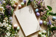 © Людмила Мазур - A beautiful arrangement featuring a blank card surrounded by vibrant flowers and pastel colored Easter eggs, perfect for festive greetings.