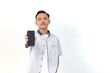 © Rifqi Muflih - Asian man wearing a shirt with a confident expression is holding a smartphone on an isolated white background.