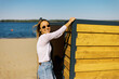 © Alexey Kuzma/Stocksy - Woman Smiling by the Beach Near a Wooden Structure on a Sunny Day