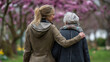 © Laura - Faceless young woman strolling with an elderly person through a spring park, soft natural lighting, defocused blooming background, outdoor senior care, intergenerational walk,