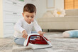 © New Africa - Child safety at home. Little boy playing with iron on floor indoors, space for text