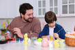 © New Africa - Easter celebration. Father and his son painting eggs at white marble table in kitchen