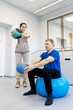 © wedmoments.stock - Male patient performing upper body rehabilitation exercises with a female therapist using exercise balls in a bright, modern rehabilitation center