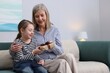 © New Africa - Little girl greeting her grandmother with gift on sofa indoors, space for text