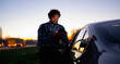 © Artcore Studio/Stocksy - Smiling man checks his mobile phone while standing by a parked car