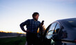 © Artcore Studio/Stocksy - Man in plaid shirt looks at smartphone while standing beside a car