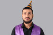© Pixel-Shot - Displeased young man with party hat on grey background. Birthday celebration