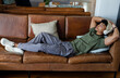 © Wavebreak Media - African American man lying on brown leather sofa at home in beanie and listening with headphones