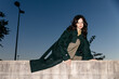 © Tania Cervian/Stocksy - Woman wearing green trench coat sitting on wall