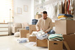 © Pixel-Shot - Young man with wardrobe boxes putting sneakers into container in dressing room