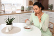 © Pixel-Shot - Young African-American woman with coffee eating cookies at table in kitchen