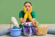 © Pixel-Shot - Tired young woman different cleaning supplies sitting on floor near green wall
