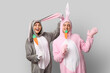 © Pixel-Shot - Beautiful young couple in bunny costume with paper carrots on grey background. Easter celebration