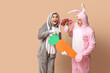 © Pixel-Shot - Beautiful young couple in bunny costume with bouquet of tulips and paper carrot on brown background. Easter celebration