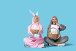 © Pixel-Shot - Beautiful young couple in bunny costume with Easter baskets sitting on blue background