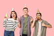 © Pixel-Shot - Young friends in funny disguise with party cones and whistles showing thumb-up gesture on pink background. April fool's day celebration