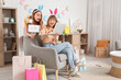 © Pixel-Shot - Surprised young women in bunny ears headbands with laptop and paper bags for Easter at home. Online shopping concept