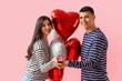 © Pixel-Shot - Young engaged couple with wedding ring and heart-shaped balloons on pink background. Valentine's Day celebration
