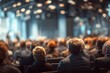 © Nuttawut - Conference Audience: A blurred and atmospheric scene of an audience gathered in a large conference hall, their focus directed towards an unseen presentation or speaker.