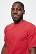 © SHOTPRIME STUDIO - Portrait of confident black man with dark skin wearing red t shirt looking at camera isolated on white background. African ethnicity, casual style and natural expression in studio lighting.