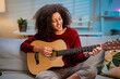 © Kawee - Latina beautiful woman playing guitar in living room at home.
