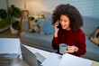 © Kawee - Latina businesswoman working and talking on mobile phone at home desk.