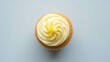 © Kamal - Overhead view of a single vanilla cupcake with swirled white lemon or vanilla buttercream frosting and zest on top, placed on a light blue or pale gray surface