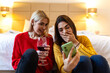 © Graphicroyalty - Two female friends looking at smartphone and laughing. Social media, communication and lifestyle concept. Young women holding a glass of wine and having fun with mobile phone in a cozy bedroom.