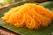 © Moddy - Delicate golden threads of a sweet Thai dessert resting on a vibrant green leaf