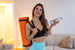 © Graphicroyalty - Ready for workout. Fitness motivation, Healthy lifestyle, Healthcare and medicine concept. Happy woman holding yoga mat and bottle of water in living room. Active girl prepared for home exercise.