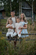 © Татьяна Зернова - A family of four stands together in a grassy field. The father is a young Caucasian man with short hair. The mother is a young Caucasian woman with long hair.