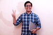 © Nurma - Southeast Asian man wearing flannel shirt standing and smiling expression happy holding laptop with giving number 12345 by hand gesture, on white isolated background.