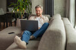 © ty - Happy young man sitting on sofa and working on laptop from home