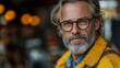 © sommersby - Close-up portrait of wise, distinguished mature man with grey beard and hair, wearing tortoiseshell glasses and vibrant yellow jacket, with softly blurred bokeh background.