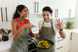 © Wavebreak Media - African American couple cooking on gas range in home kitchen in olive aprons, sampling wooden spoon