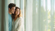 © Broccolini - happy young couple looking out the window in bright spring morning, smiling man and woman opening white curtains in sunny living room, lifestyle scene of cheerful couple enjoying daylight at home
