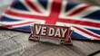 © Stocker - Victory in europe day pin badge resting on union jack flag fabric surface commemorating historical celebration of peace and end of world war two with classic british military style