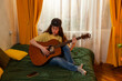 © _KUBE_ - Caucasian young woman student learning guitar on a bed at home. Indoor music practice. Creativity and education. Top view
