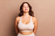 © Inai - Studio portrait of a plus size woman in a light top against a beige background. Body positivity, natural beauty and self confidence concept with minimalist composition and clean copy space.