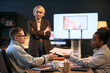 © DragonImages - Caucasian young adult man handing printed photo to Black young adult woman while middle aged Caucasian woman standing in background, business meeting taking place in modern office setting