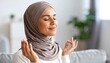 © Vom Baty - Calm Woman in Hijab Meditating in Bright Living RoomDescription: Portrait of a peaceful woman in a headscarf practicing mindfulness with eyes closed. Represents mental wellness, stress relief, and sp