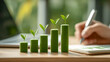 © Alex Alex - The columns of the green histogram with young plant shoots on top are arranged from bottom to top. In the background, a hand with a pen is writing something in a notebook.