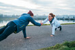 © Soloviova Liudmyla - Active young Caucasian couple in athletic jackets and beanies performing high plank variations while giving each other a high-five on a paved riverside path during an outdoor fitness workout sunrise