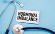 © Pawel - HORMONAL IMBALANCE text on a white card placed next to a stethoscope on a blue medical background.