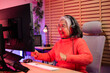 © NVB Stocker - excited senior eldery Asian woman with headphones streamer playing video game using desktop computer at gaming room at home. colorful neon background