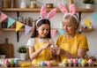 © Shihab - A woman and a girl wearing bunny ears and decorating easter eggs together in a kitchen with shelves